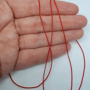 May include: Red elastic cord, shown in a hand, is a versatile crafting material.