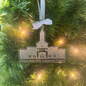 May include: White acrylic ornament featuring a silhouette of the Grand Junction Colorado Temple. The ornament is hanging on a Christmas tree.