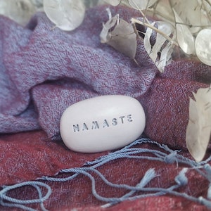 Puede incluir: Piedra blanca con la palabra "Namaste" inscrita en ella, descansando sobre un fondo de tela azul y burdeos.