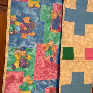 May include: Two baby quilts, one with a patchwork design of blue, green, and pink squares, and the other with a colorful design of bears and stars.