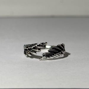 May include: A silver ring with a detailed design of two wings.