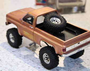 May include: A brown toy pickup truck with a spare tire in the bed. The truck has a black bed liner and a chrome bumper. The truck is sitting on a light gray surface.