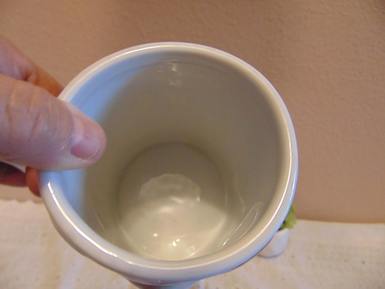 May include: A white ceramic mug with a smooth, glossy interior finish and a cylindrical shape. The mug features a simple, clean design with a rounded rim and a deep, hollow center, showcasing the plain white surface of the vessel's interior.