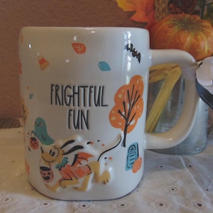 May include: A white ceramic mug featuring the text FRIGHTFUL FUN in black lettering. The mug displays a raised, colorful illustration of a dog wearing a costume, surrounded by orange trees, a tombstone, a bat, and falling autumn leaves.