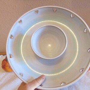 May include: A light blue ceramic serving platter with a central dip bowl. The platter has a ring of heart-shaped cutouts around the edge. The piece has a glossy finish and is suitable for serving snacks or appetizers.