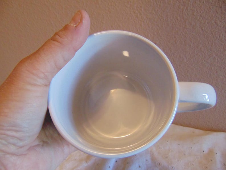 May include: A plain white ceramic mug with a smooth, glossy finish and a rounded handle. The interior of the mug is entirely white and empty, showing a clean, circular opening. The mug is designed with a simple, functional structure for holding liquids.