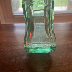 May include: A vintage green glass bottle with the text "TRADE MARK REG IN US PATENT" embossed on the upper portion. The number "62-33" is visible near the base. The bottle has a classic, curved shape.