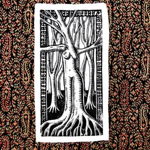 Puede incluir: Un grabado en linóleo rectangular en blanco y negro sobre tela que presenta una figura central que fusiona la forma de un torso humano con el tronco y las ramas de un árbol, rodeada por un bosque de árboles estilizados dentro de un borde decorativo.