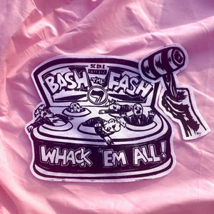 Könnte beinhalten: Ein schwarz-weißer Aufkleber, der ein Spiel im Stil von Hau-den-Lukas mit dem Text BASH THE FASH und WHACK EM ALL zeigt. Das Design zeigt eine Hand, die einen Hammer über Figuren in Löchern hält, mit einem Punktezähler und einem Antifa-Symbol.
