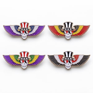 May include: Four enamel pins featuring a skull wearing a top hat with stars and stripes, sunglasses, and large feathered wings. Each pin displays a different color scheme: red, white, blue, and purple; red, yellow, and black; green, yellow, and purple; or black, white, and red.