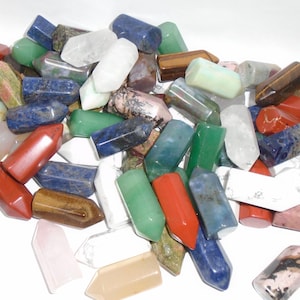 May include: A collection of colorful, polished, pointed gemstone wands. The wands are made of various types of stones, including amethyst, rose quartz, tiger's eye, and clear quartz.