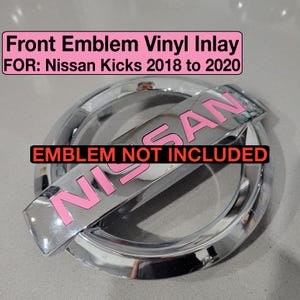 May include: A chrome car emblem with a pink vinyl inlay that says "NISSAN". The text "Front Emblem Vinyl Inlay FOR: Nissan Kicks 2018 to 2020" is in a pink box at the top of the image. The text "EMBLEM NOT INCLUDED" is in a red box at the bottom of the image.
