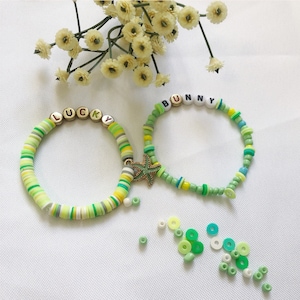 May include: Two colorful beaded bracelets with the words "LUCKY" and "BUNNY" spelled out in white letters. The bracelets are green, white, and yellow and feature a gold starfish charm.