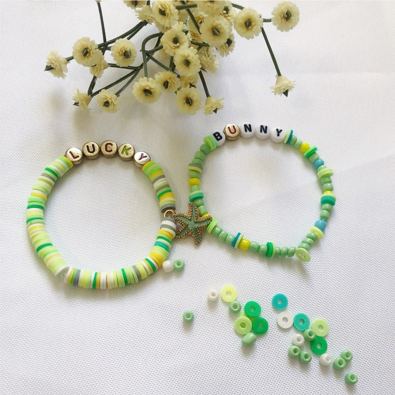 May include: Two colorful beaded bracelets with the words "LUCKY" and "BUNNY" spelled out in white letters. The bracelets are green, white, and yellow and feature a gold starfish charm.