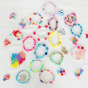 May include: A collection of colorful beaded bracelets with various charms and letters. The bracelets are made with different colored beads, including pink, blue, green, yellow, and white. Some of the charms include hearts, stars, and letters. The bracelets are arranged on a white surface.