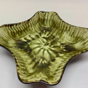 May include: A green and brown ceramic serving dish with a wavy, star-shaped rim. The dish has a swirl pattern in the centre.