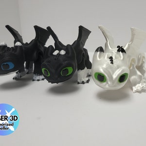May include: Three 3D printed figurines of Toothless, the Night Fury dragon from the How to Train Your Dragon franchise. The figurines are in black, white, and a light gray color. The figurines have green eyes and white markings.