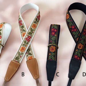 May include: Four camera straps with floral embroidery. Straps A and B have a cream background with orange and red flowers. Straps C and D have a black background with orange and red flowers. All straps have leather ends and metal rings.