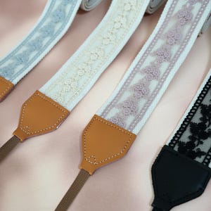 May include: Four camera straps with different lace designs. The straps are white with different colored lace trim. The straps have brown leather adjustable pieces.