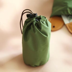 May include: A small green drawstring bag with a black plastic toggle closure. The bag is made of a lightweight, water-resistant material.