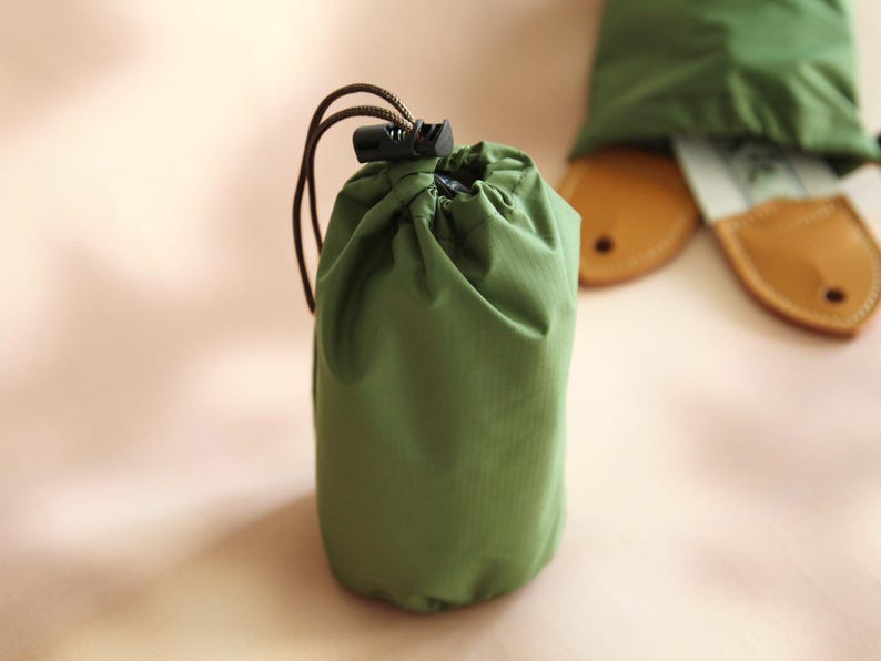 May include: A small green drawstring bag with a black plastic toggle closure. The bag is made of a lightweight, water-resistant material.