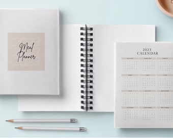 May include: Two spiral bound notebooks, one with a beige cover and the text "Meal Planner 2023" and the other with a white cover and the text "2023 CALENDAR".