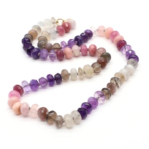 May include: A gemstone necklace with a gold clasp, featuring a spectrum of colours. The necklace showcases a gradient of pink, purple, brown, and white beads. The beads are in various shapes and sizes, creating a unique and eye-catching design.