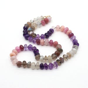 May include: A multi-colored gemstone necklace with a gold clasp. The necklace features a variety of polished stones in shades of pink, purple, brown, and white. The stones are strung together, creating a beautiful and unique piece of jewelry.