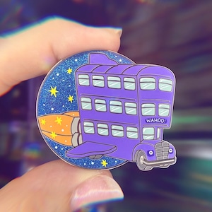 May include: Purple and blue enamel pin of a double-decker bus with a rocket booster attached to the back. The bus has the word "WAHOO!" printed on the side. The pin is set against a sparkly blue background with yellow stars.