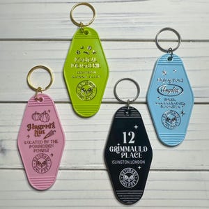 May include: Five colorful keychains with a Harry Potter theme. Each keychain features a different location from the Harry Potter universe, including Hagrid's Hut, the Magical Menagerie, 12 Grimmauld Place, and the Flying Ford Anglia. Each keychain has a gold or silver owl charm with the words "Return by Owl Post".