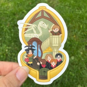 Pode incluir: Um adesivo recortado com uma ilustração de desenho animado de uma sala de aula com um esqueleto de dragão, um professor em um pódio e alunos. O design é emoldurado por uma borda dourada com fundo verde claro e personagens.