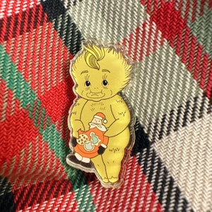 May include: A yellow, cartoon-style figure with a spiky yellow hairdo is holding a small, red, cartoon Santa Claus figure. The Santa Claus figure is holding a plate of cookies. The figure is standing on a red and white plaid background.
