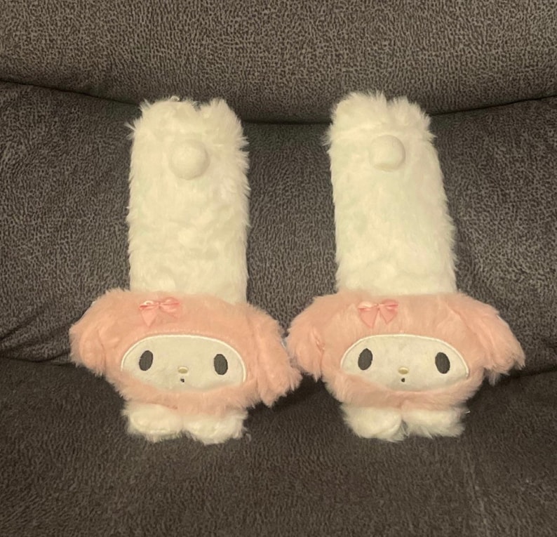 May include: Two white plush hand warmers with pink bunny faces and pink bows. The bunny faces have black eyes and a pink nose.