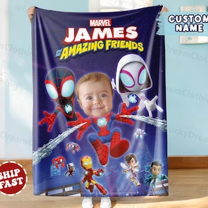 Puede incluir: Una manta azul marino de Marvel con el texto "JAMES and his AMAZING FRIENDS". La manta muestra ilustraciones de personajes de Spider-Man y la cara de un beb&eacute;. La manta est&aacute; sujeta por una persona.