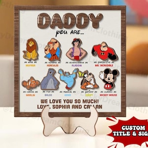 May include: A wooden sign with a brown frame and a white background. The sign says "Daddy you are..." and features a collage of Disney characters with text describing their qualities. The sign also says "We love you so much! Love, Sophia and Caelan".