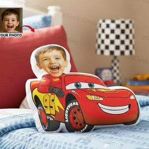 May include: A custom pillow featuring a child's face integrated into a red Lightning McQueen car design. The pillow has a white background, with the child's face replacing the driver. The car has the number 95 and the word "LIGHTYEAR" on the tire.