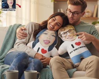 May include: A couple sits on a couch, holding custom-made plush dolls with faces printed on them. One doll has the text "I ❤️ MY GIRLFRIEND". The dolls are white with blue and red accents. The image includes a photo of a woman.