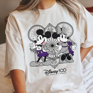 May include: A white t-shirt with a black and white illustration of Mickey Mouse and Minnie Mouse. The illustration is surrounded by a geometric design. The text "Disney 100 100 YEARS of WONDER" is printed below the illustration.