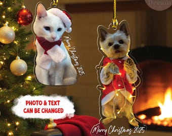 May include: Christmas ornaments featuring a white cat and a small dog, both dressed in festive attire. The cat wears a Santa hat and scarf, while the dog is in a red coat with lights. Each ornament has the text "Merry Christmas 2025".