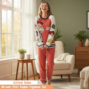 Puede incluir: Conjunto de pijama color coral con una parte superior estilo raglán con mangas blancas y cuello negro. La parte superior tiene un gráfico de un personaje de dibujos animados con el nombre "Jess". Los pantalones a juego tienen puños a rayas blancas y negras.