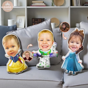 May include: Three custom-made plush pillows featuring children's faces. One pillow is designed as Snow White in a yellow dress, another as Buzz Lightyear, and the third as Elsa in a blue dress. The pillows are on a gray couch.