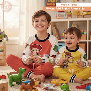 Puede incluir: Conjuntos de pijama raglán con estampado integral con personajes de Toy Story. Un conjunto es rojo con un gráfico de Jessie, el otro es amarillo con un gráfico de Woody. Los pijamas tienen mangas largas y los llevan dos niños. El texto "Custom Name" y "All-over Print Raglan Pajamas Set" es visible.