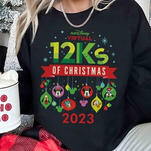 May include: Black sweatshirt with a graphic of Mickey Mouse and other Disney characters hanging from ornaments. The text "runDisney VIRTUAL 12KS OF CHRISTMAS 2023" is printed on the sweatshirt.