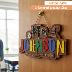 May include: A custom 2 layered wooden sign hanging on a door, featuring the text Mrs. JOHNSON in colorful letters, a small circular 9 3/4 emblem, a wizard hat, and a broomstick illustration, all suspended by a thin twine string from a metal hook.