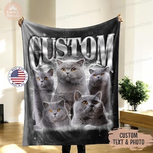 May include: A black fleece blanket with a silver "CUSTOM" text and a graphic of five gray British Shorthair cats. The blanket is made in the USA.