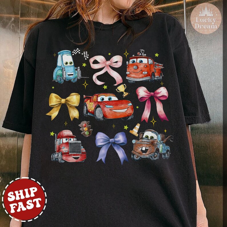 May include: Black t-shirt with a colorful cartoon design featuring cars from the Disney Pixar movie Cars. The design includes Lightning McQueen, Mater, and other characters. The shirt has a crew neck and short sleeves.
