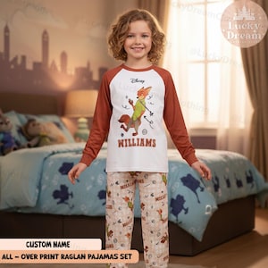 Peut inclure: Un ensemble de pyjamas Disney pour enfant. Le haut blanc a des manches marron et un dessin de renard de dessin anim&eacute; avec le nom "WILLIAMS" en dessous. Le pantalon de pyjama a un motif de renard r&eacute;p&eacute;t&eacute;. Le texte "ALL-OVER PRINT RAGLAN PAJAMAS SET" est en bas.