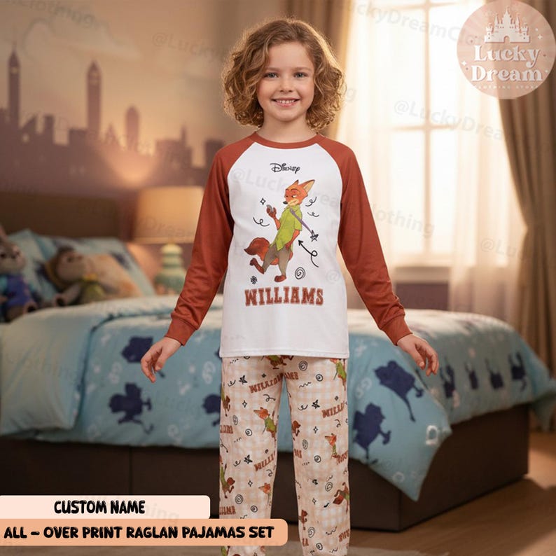 Peut inclure: Un ensemble de pyjamas Disney pour enfant. Le haut blanc a des manches marron et un dessin de renard de dessin anim&eacute; avec le nom "WILLIAMS" en dessous. Le pantalon de pyjama a un motif de renard r&eacute;p&eacute;t&eacute;. Le texte "ALL-OVER PRINT RAGLAN PAJAMAS SET" est en bas.