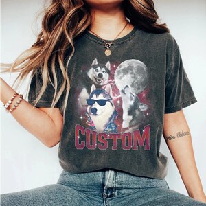 May include: A dark gray t-shirt with a graphic print of three cartoon huskies in front of a full moon. The huskies are wearing sunglasses and one is wearing a Hawaiian shirt. The text "CUSTOM" is printed in red below the huskies.