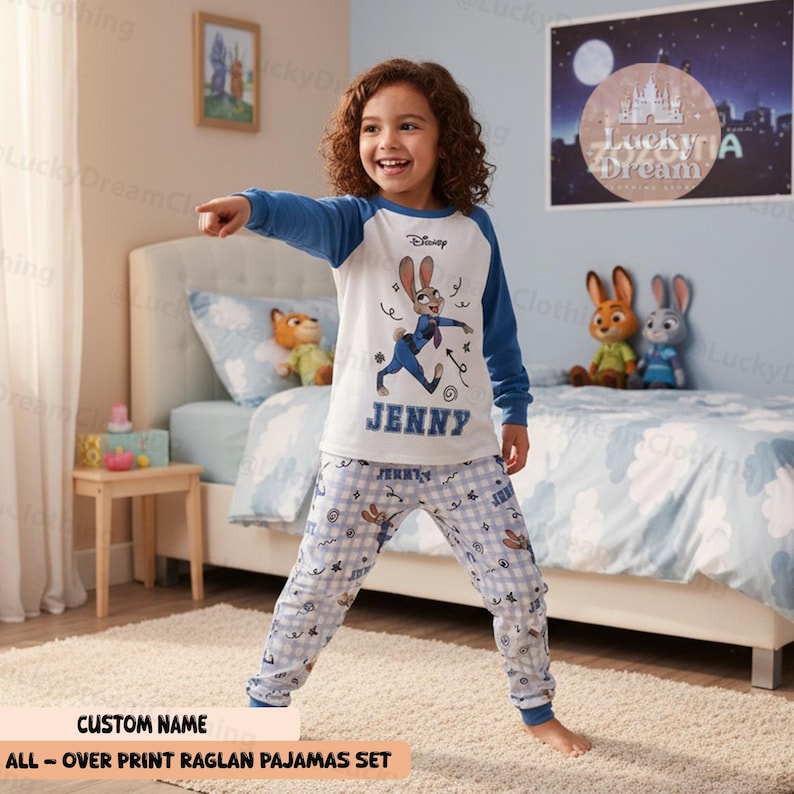 Peut inclure: Un ensemble de pyjama bleu et blanc pour enfant, avec un personnage de dessin anim&eacute;. Le haut a des manches bleues et un motif graphique, avec le nom "JENNY" imprim&eacute; en dessous. Le bas de pyjama est bleu clair avec un motif &agrave; carreaux et des d&eacute;tails de personnage.